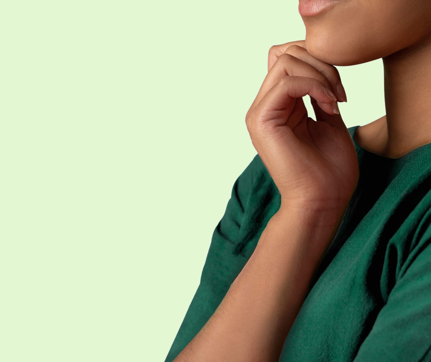 Vrouw in een groen shirt met haar hand onder haar kin, tegen een lichtgroene achtergrond