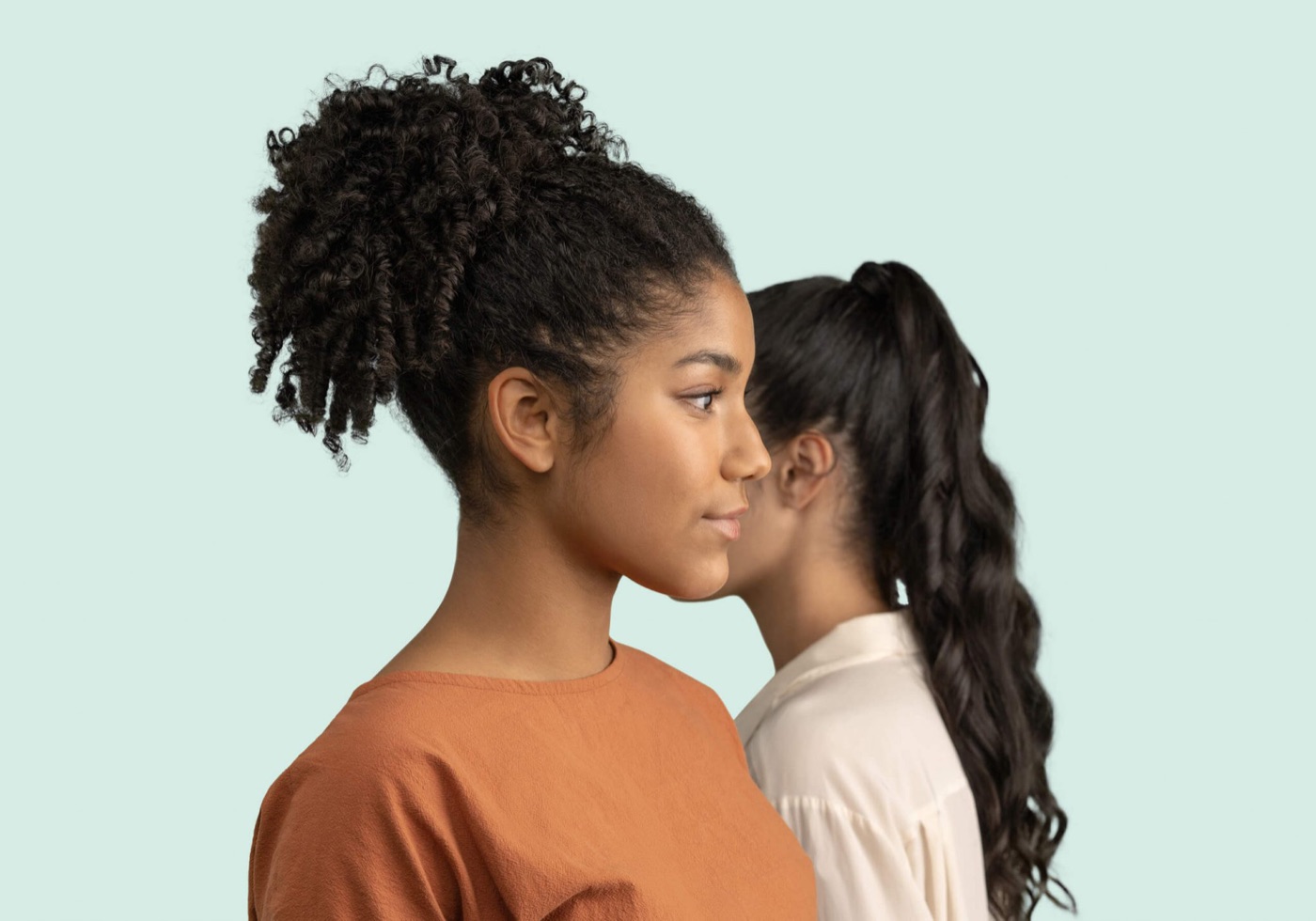Twee jonge vrouwen staan dicht bij elkaar en kijken dezelfde kant op, tegen een mintgroene achtergrond
